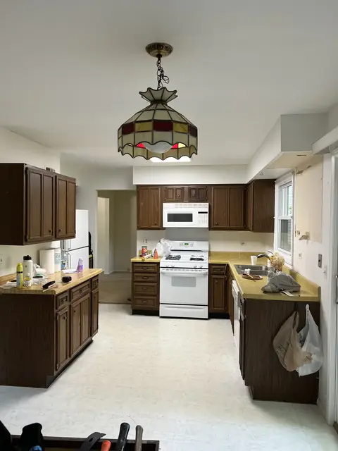 Kitchen before remodeling with dark wood cabinets, white appliances, and the original flooring