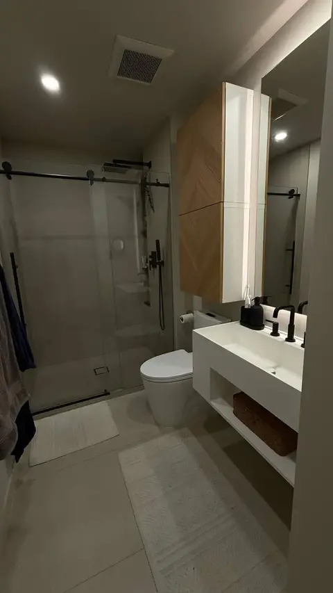 Remodeled bathroom with a frameless glass shower, floating oak vanity, and illuminated mirror