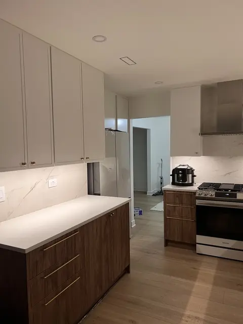 Remodeled kitchen corner with full-height white cabinetry, walnut drawers, and under-cabinet lighting